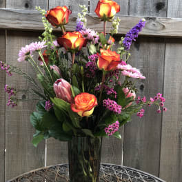 Tall bouquet of orange-red roses and pink flowers in a glass vase