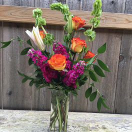 Orange and yellow roses in a clear glass vase with magenta flowers