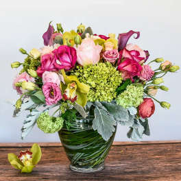 Mixed bouquet of pink roses, green hydrangea, and orchids in a clear glass vase