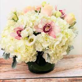 Low round arrangement of white hydrangeas with pale pink roses and orchids in a glass vase