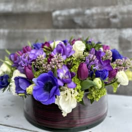 Purple and white mixed flower arrangement in a round glass vase