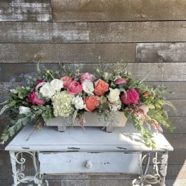 Long floral arrangement of pink, coral, and white roses in a white container