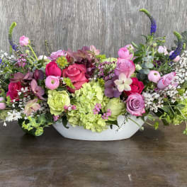 Low floral centerpiece with pink and purple roses in a white bowl vase