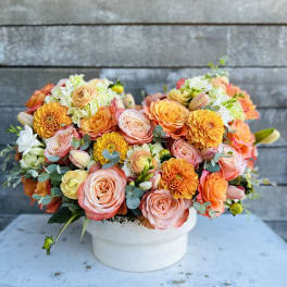 Peach and orange mixed flower arrangement in a white vase