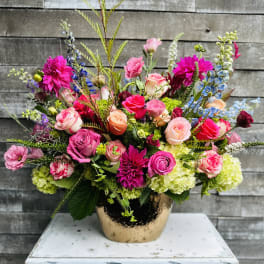Bright mixed bouquet in a gold vase with pink, peach, and blue flowers
