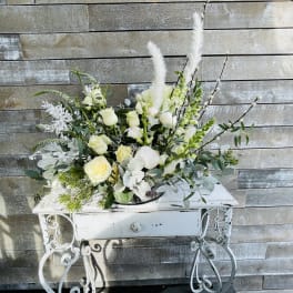 White rose arrangement with tall feather accents in a white metal stand