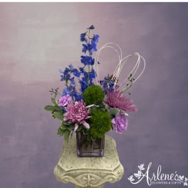 Purple and blue floral arrangement in a square glass vase