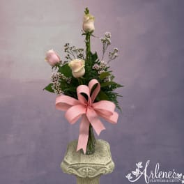 Pink and white roses in a glass vase with a large pink ribbon