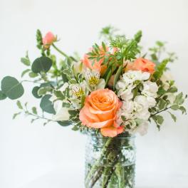 Peach roses and white flowers in a clear glass jar vase