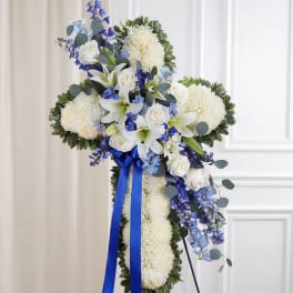 Standing floral cross with white flowers and blue accents on an easel