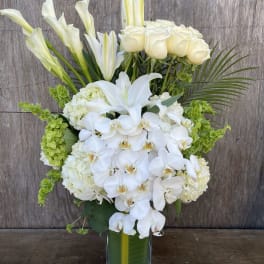 White orchids, roses, lilies, and green hydrangeas in a glass vase