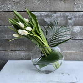 White tulips arranged in a round glass vase with palm leaves