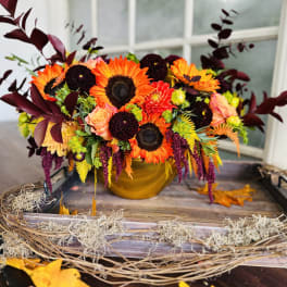 Autumn bouquet with sunflowers, orange blooms, and burgundy foliage in a gold vase