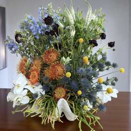 Mixed floral arrangement with blue, orange, white, and yellow blooms in a white vase