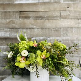 Green floral arrangement in a white vase with orchids and succulents