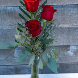 Three red roses in a clear glass vase with greenery