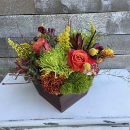 Mixed floral arrangement in a dark wooden container with roses and chrysanthemums