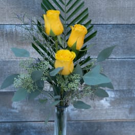 Three yellow roses in a clear glass vase with mixed greenery
