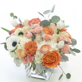 Bouquet of peach, orange, and white flowers in a clear glass vase