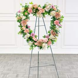 Heart-shaped floral wreath on a metal stand with pink and white blooms