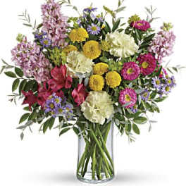 Mixed bouquet of pink, yellow, white, and purple flowers in a glass vase