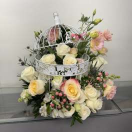 White roses and pink lisianthus arranged in a decorative white birdcage.