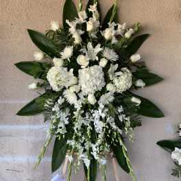 White funeral spray with roses, lilies, and orchids on an easel