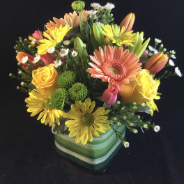 Mixed bouquet of yellow, orange, pink, and white flowers in a green striped vase