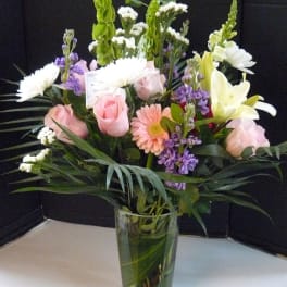 Mixed bouquet of pink roses, white lilies, and purple flowers in a glass vase
