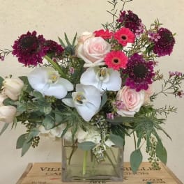 Mixed bouquet with pink roses, white orchids, and magenta blooms in a glass vase