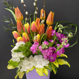 Bouquet of orange tulips, white hydrangeas, and purple flowers in a lavender vase