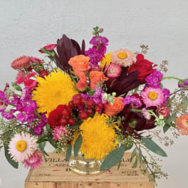 Colorful mixed bouquet in a clear glass vase with yellow, pink, red, and peach blooms.