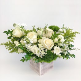 White roses and small white flowers in a square vase with green accents