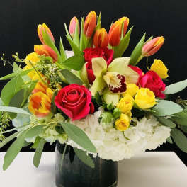Mixed bouquet of tulips, roses, orchids, and white hydrangeas in a black vase
