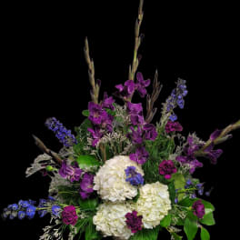 Purple and blue flowers arranged with white hydrangeas in a vase