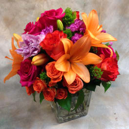 Bright mixed bouquet in a clear square vase with roses and lilies