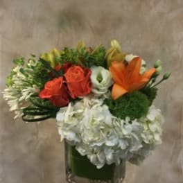Bouquet of orange and red roses with white blooms in a square glass vase