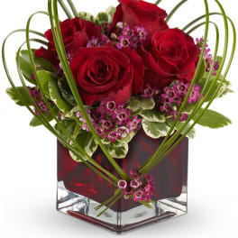 Red roses and purple accent flowers in a square glass vase
