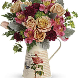 Bouquet of peach roses and burgundy flowers in a decorative pitcher vase
