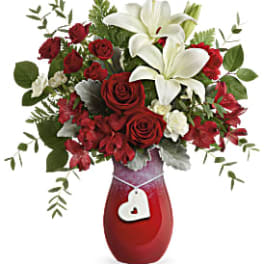 Red roses and white lilies in a red vase with a heart tag