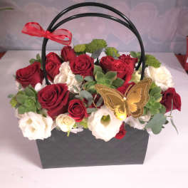 Red and white roses in a black handled basket with a butterfly decoration