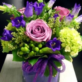 Pink and purple bouquet in a square glass vase with a purple ribbon