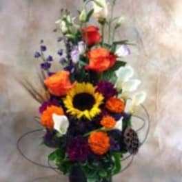 Tall colorful floral arrangement in a black vase with a sunflower and calla lilies