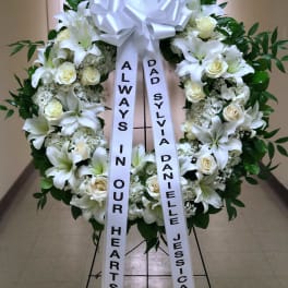 White funeral wreath with lilies, roses, and a large bow on a stand