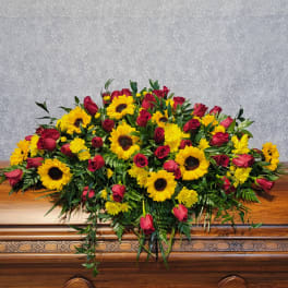 Large floral spray with red roses and yellow sunflowers on a wooden casket