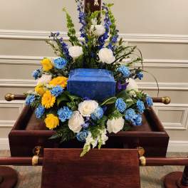 Funeral casket spray with white, blue, and yellow flowers
