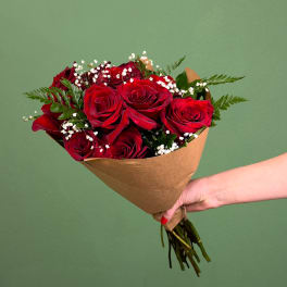 Handheld bouquet of red roses wrapped in brown paper against a green background