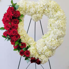 Heart-shaped floral wreath with white hydrangeas and red roses on a stand