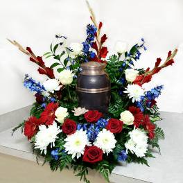 Floral funeral urn arrangement with red, white, and blue flowers around a dark urn