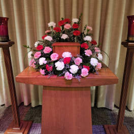Symmetrical carnation arrangement around a wooden urn on a podium